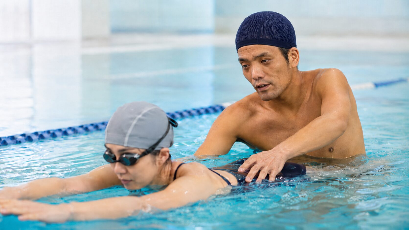 コーチが水中で成人スイマーにほう助を行いながら指導している様子